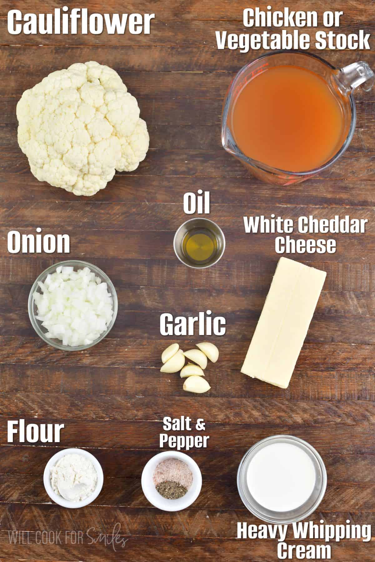 labeled ingredients to make cheesy cauliflower soup on a wooden background.