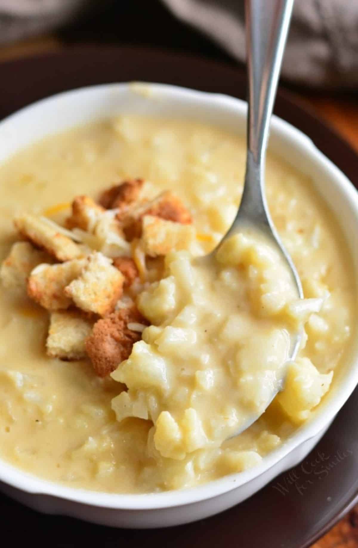 spooning cauliflower cheese soup topped with croutons and pulling it out from the bowl.