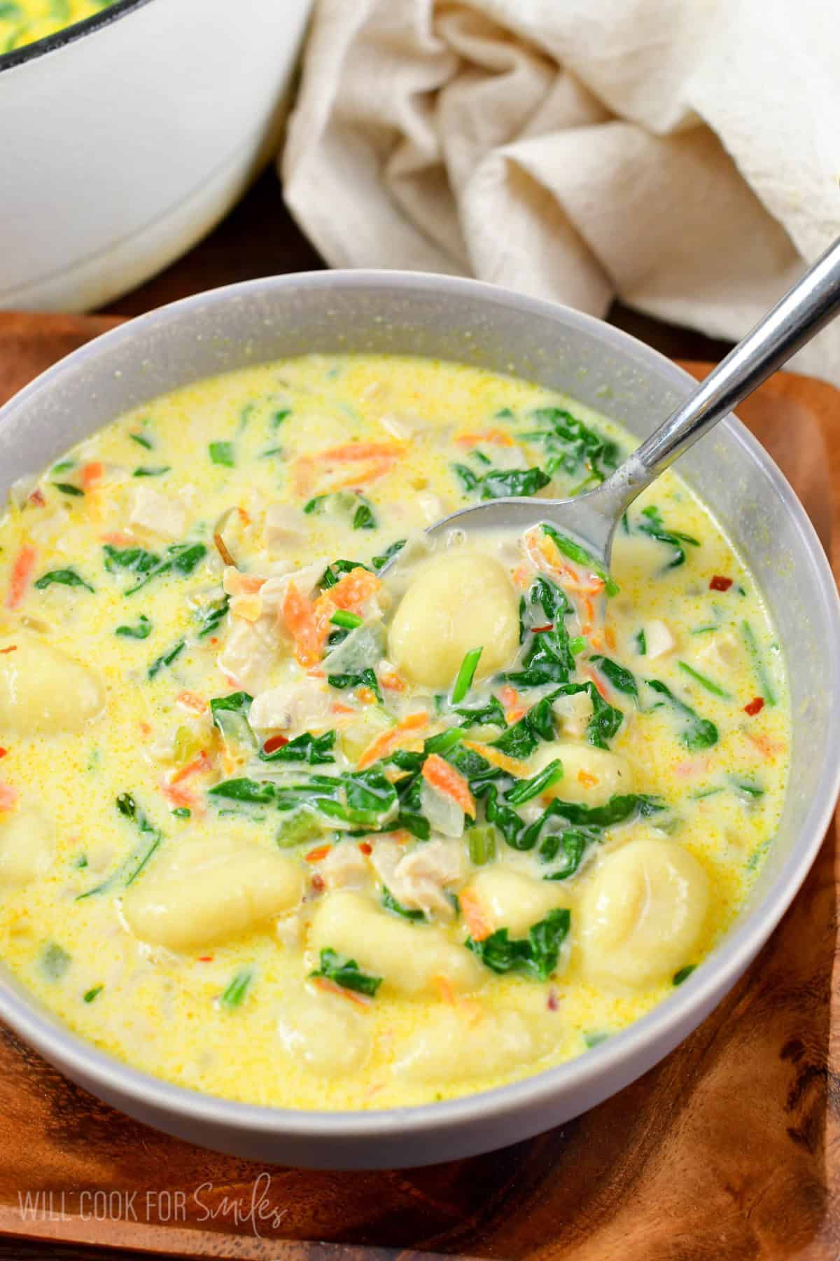 stirring the creamy gnocchi soup in a grey bowl.