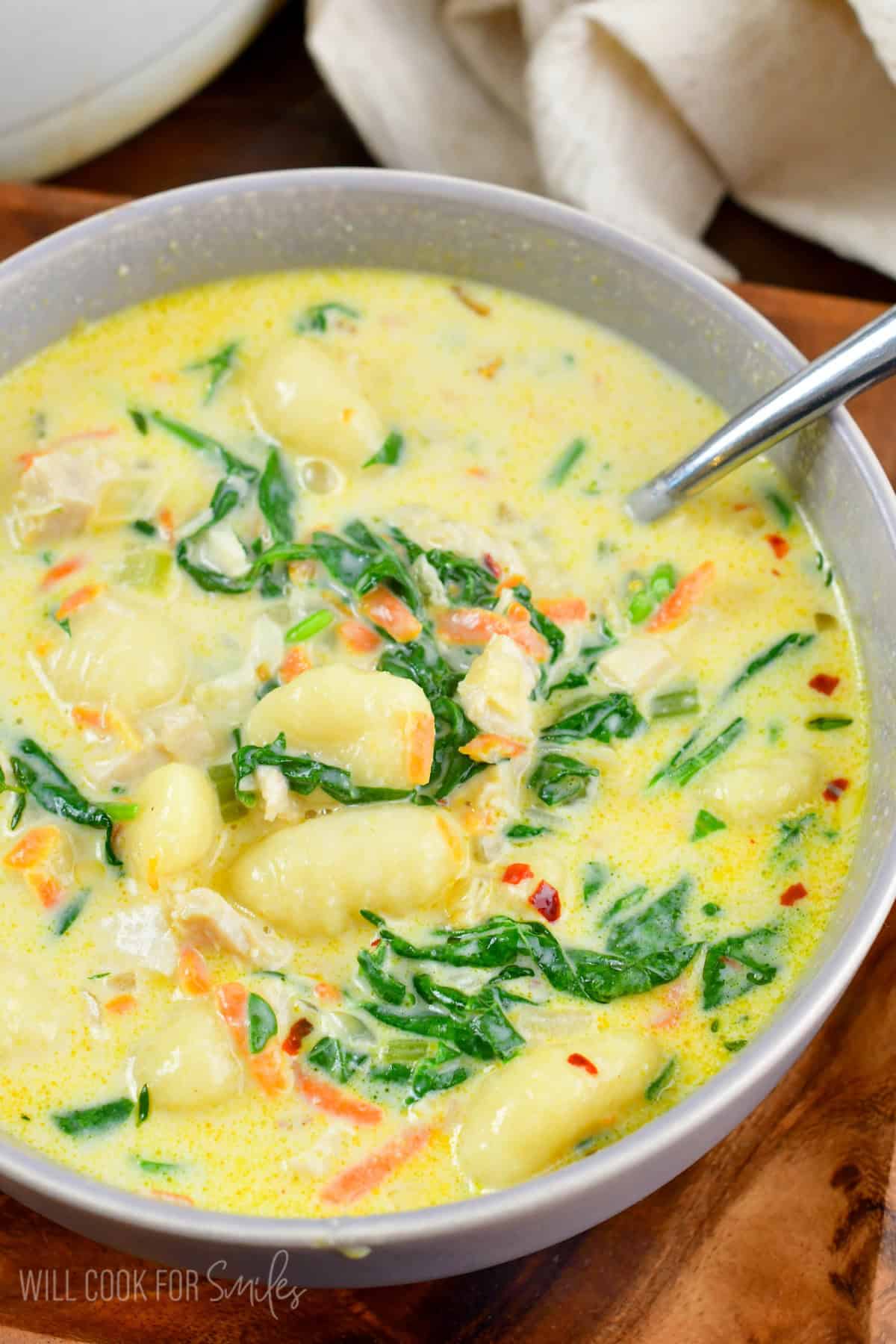 a bowl full on Creamy Chicken Gnocchi Soup with a spoon on a wooden plate.