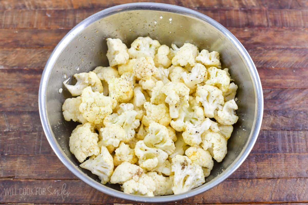 chopped cauliflower florets mixed with seasoning in a mixing bowl.