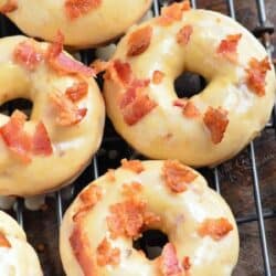 Maple bacon donuts on a wire rack on a wood surface.