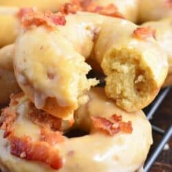 maple bacon donuts stacked on a wire rack with one broken so you see the inside.