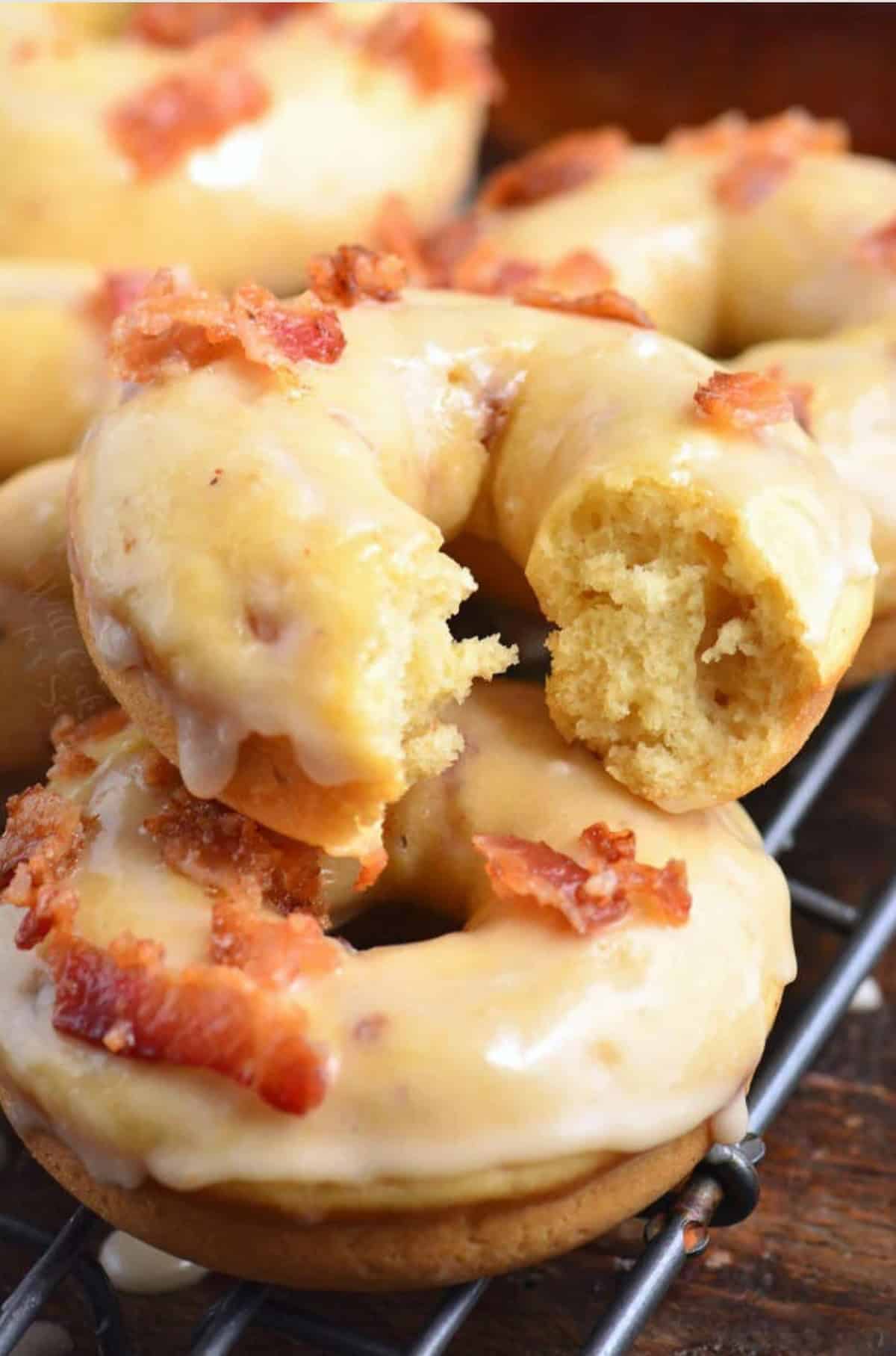 maple bacon donuts stacked on a wire rack with one broken so you see the inside.