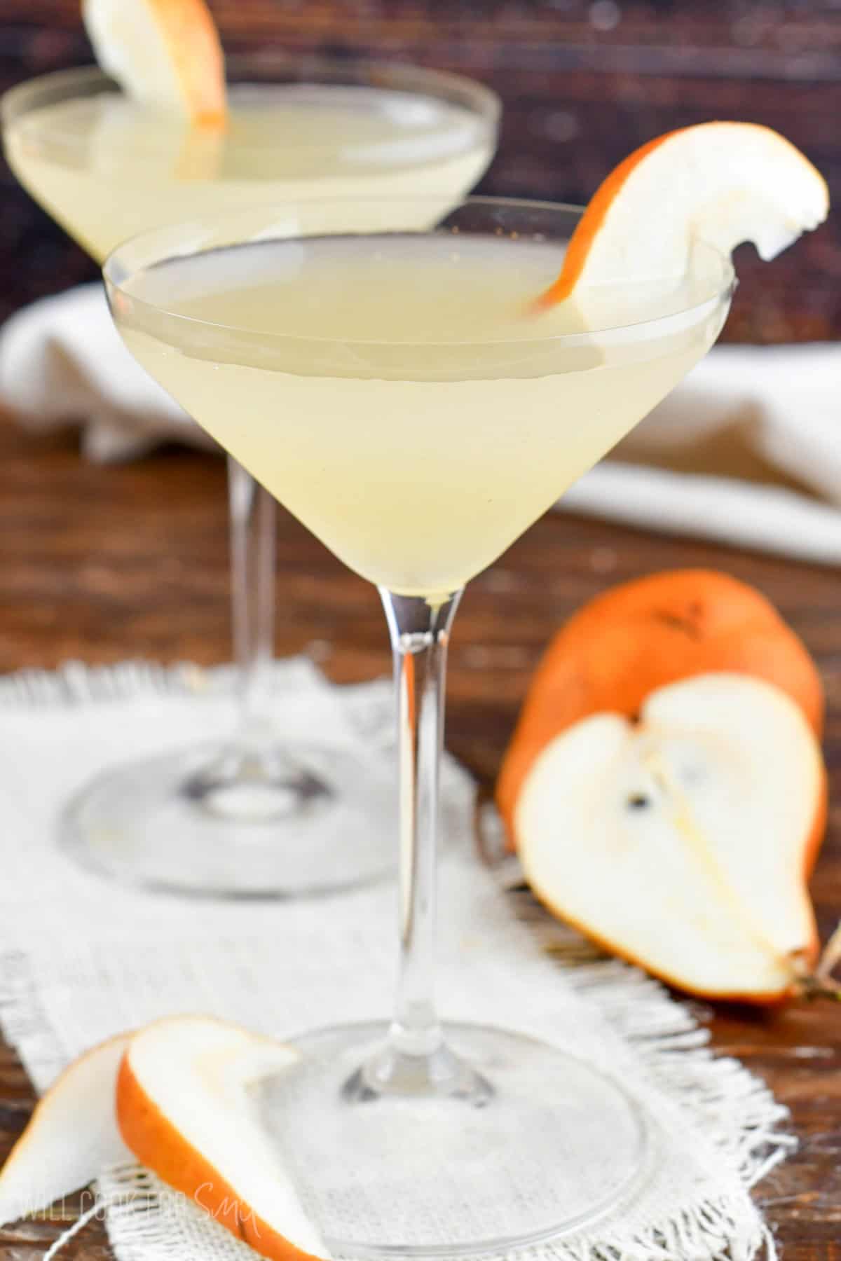 tall martini glass with pear martini and pears around the glass.