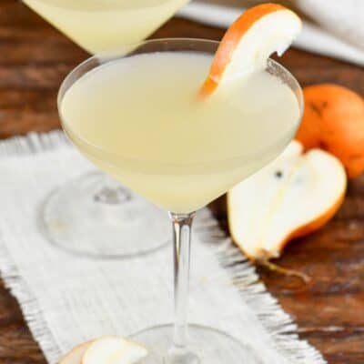 two martini glasses filled with pale yellow pear martini and garnishes with pear slices.