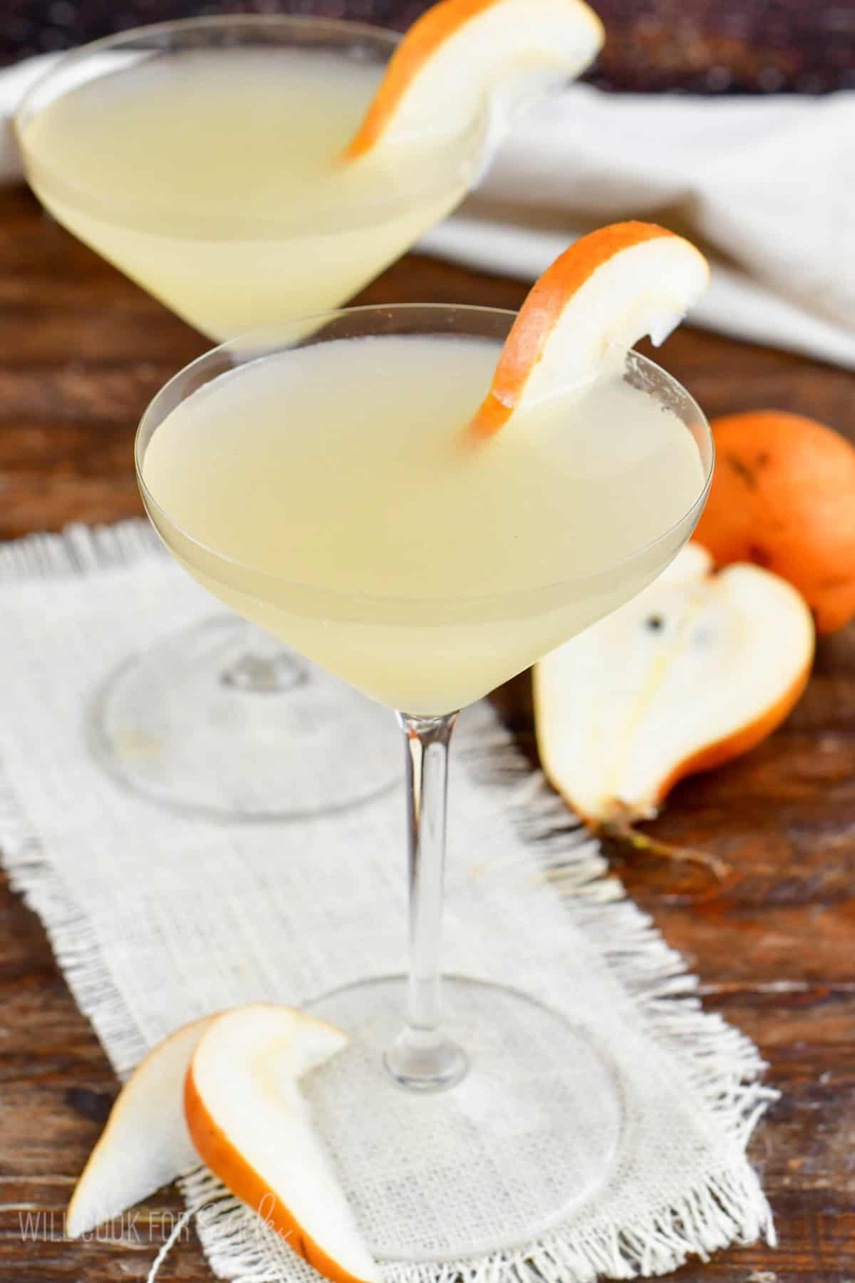 two martini glasses filled with pale yellow pear martini and garnishes with pear slices.