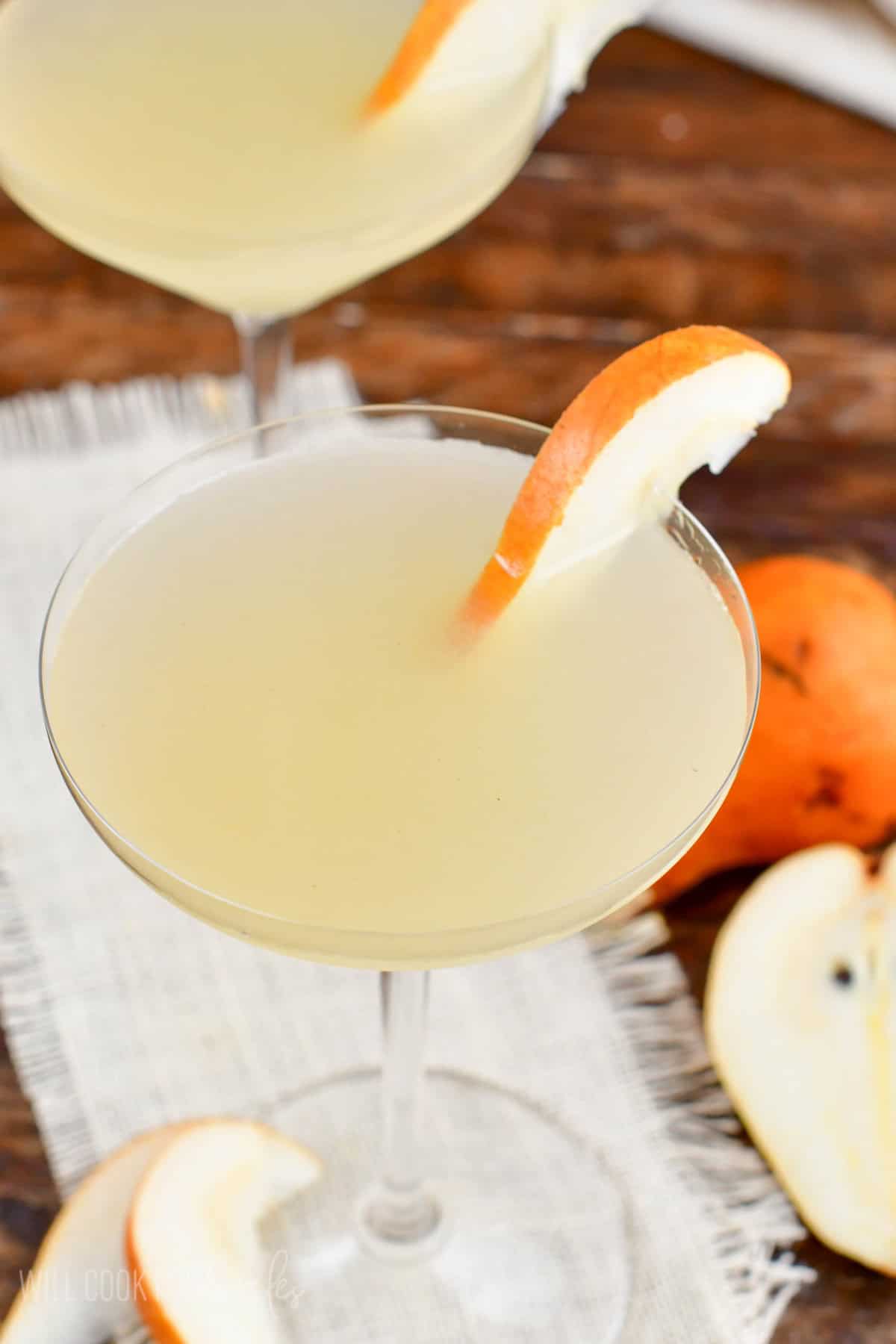 pear martini in a martini glass with pear slices and more pears around.