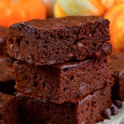 three sliced pumpkin brownies stacked up on parchment paper and chocolate chips around it.