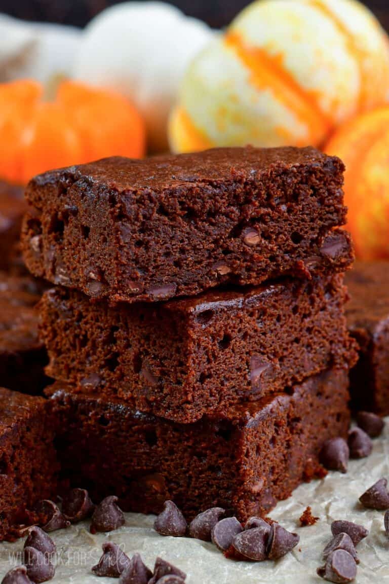 three sliced pumpkin brownies stacked up on parchment paper and chocolate chips around it.