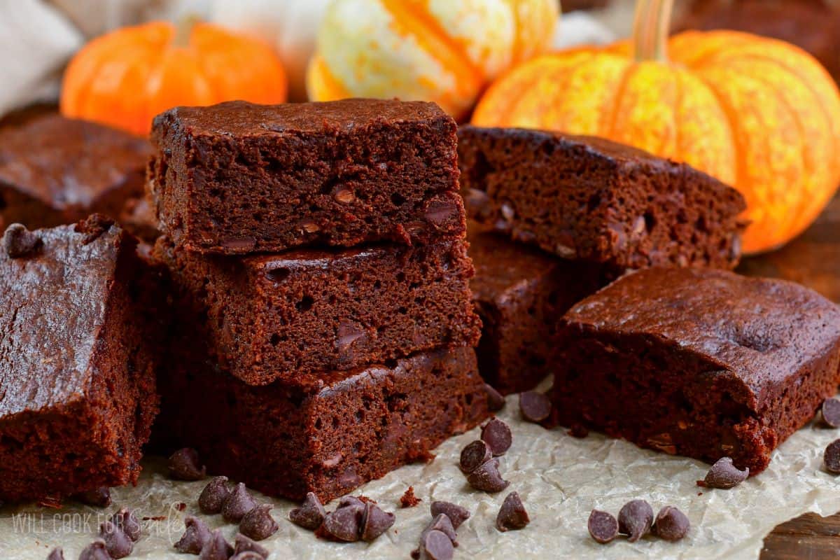 Pumpkin brownies stacked up on parchment paper with chocolate chips spread around it.