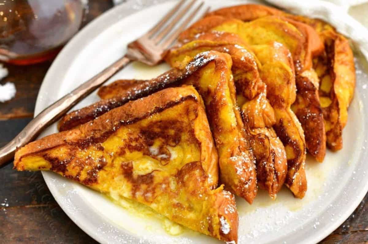 Pumpkin French toast slices on the plate cut in half and stacked on the plate with butter and powdered sugar.