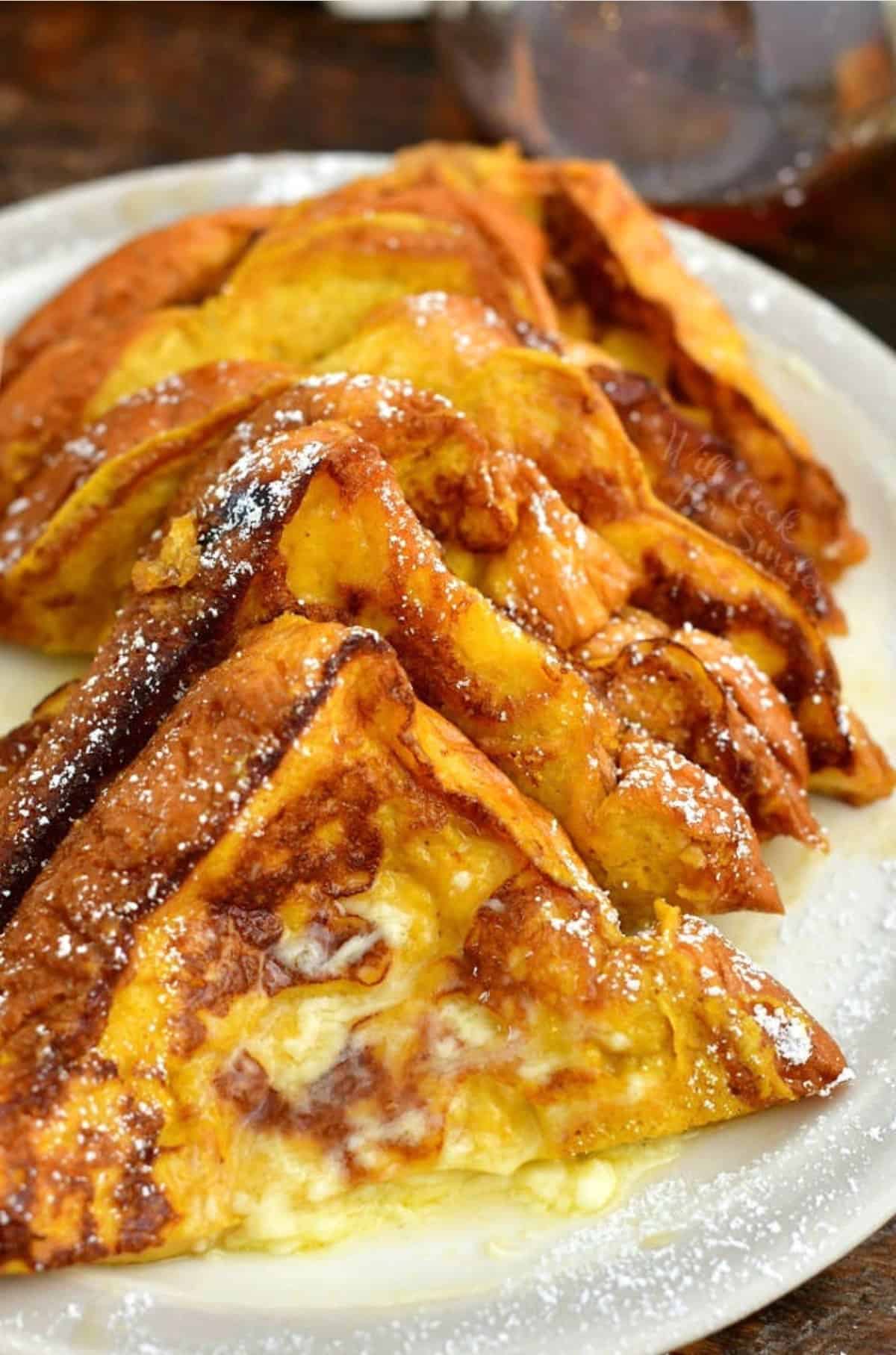 Pumpkin French toast slices cut in half and stacked on the plate with butter and powdered sugar.