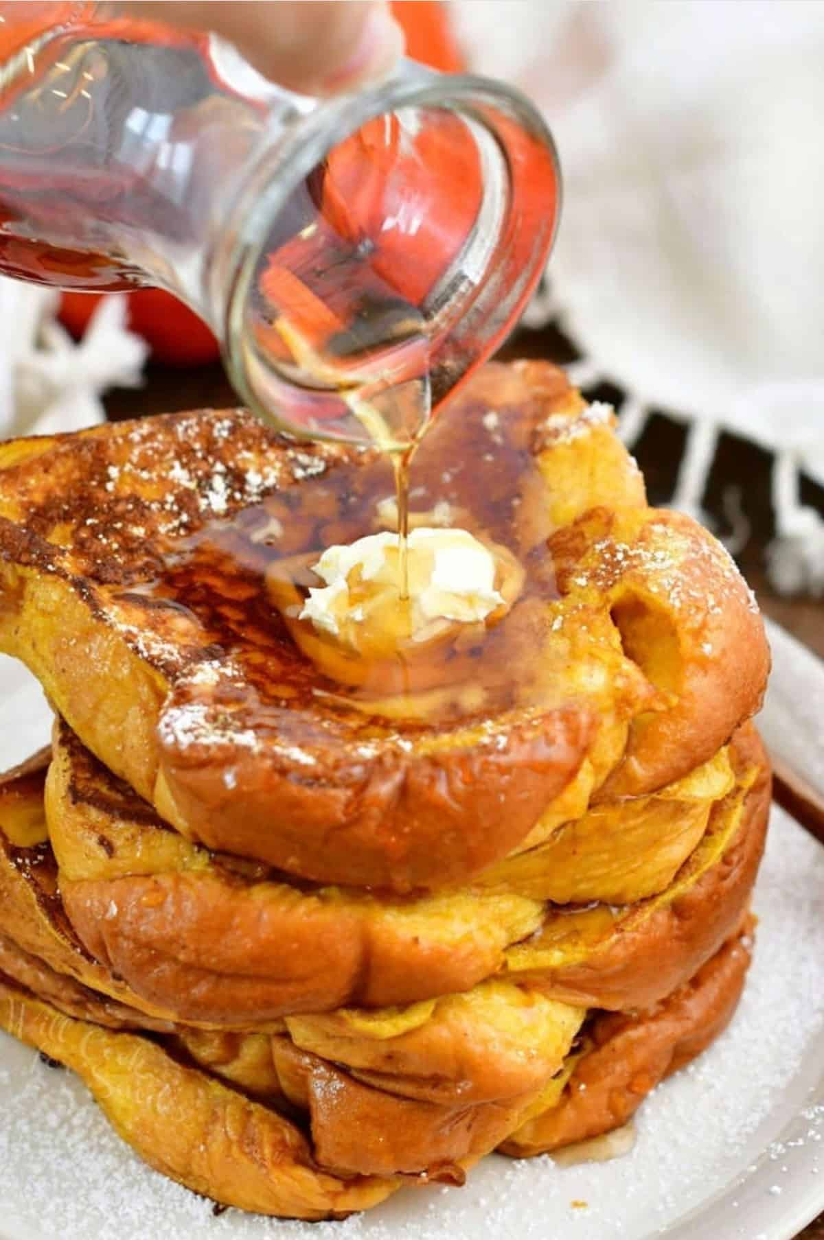 pouring maple syrup over stacked pumpkin French toast slices on the plate.