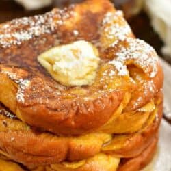 several slices of pumpkin French toast stacked on the plate topped with butter and powdered sugar.