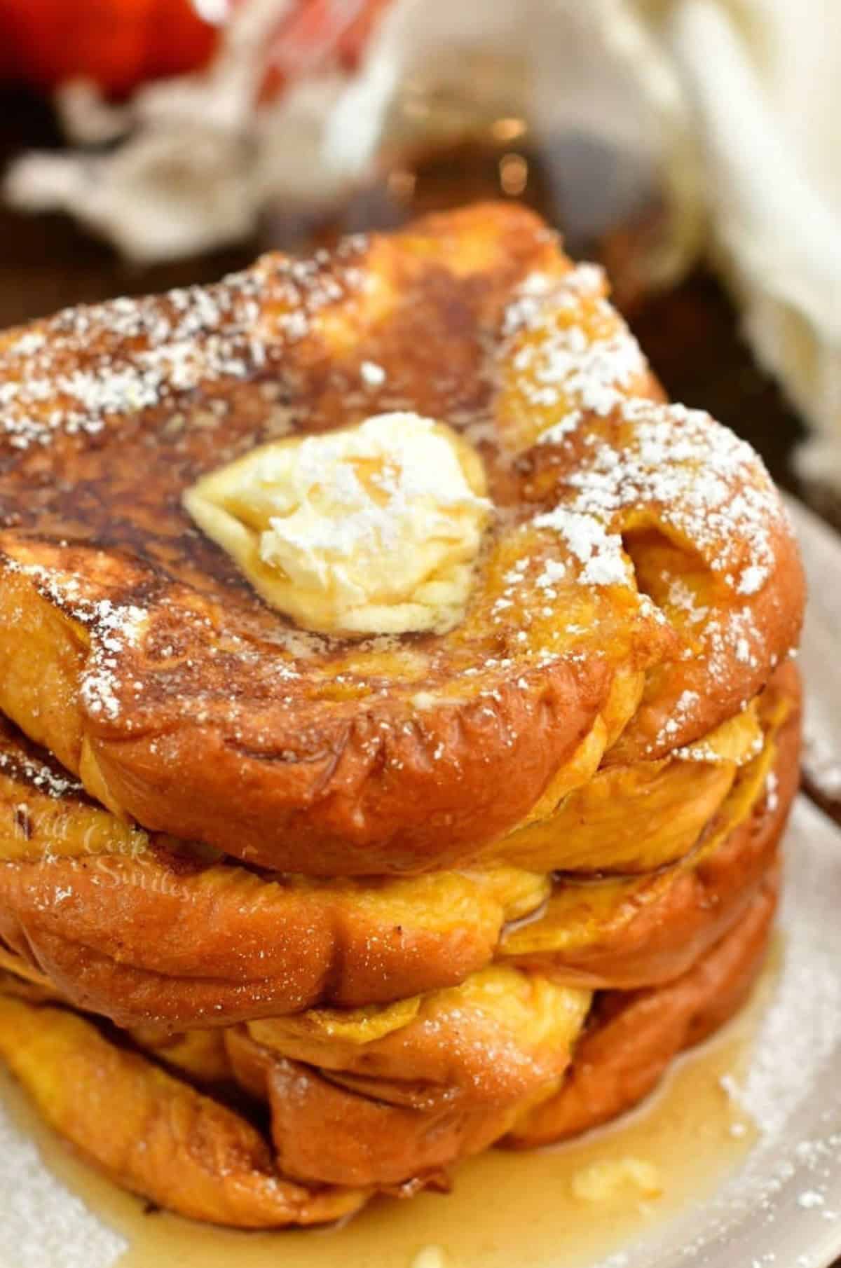 several slices of pumpkin French toast stacked on the plate topped with butter and powdered sugar.