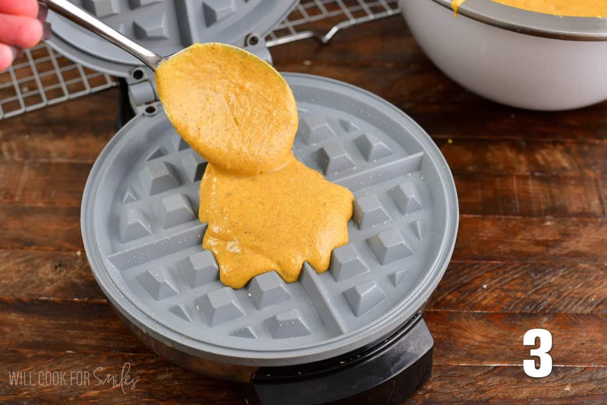 Spooning waffle batter into a waffle maker.