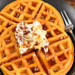 Two waffles on a plate with whipped cream and nuts on top and a fork to the right.