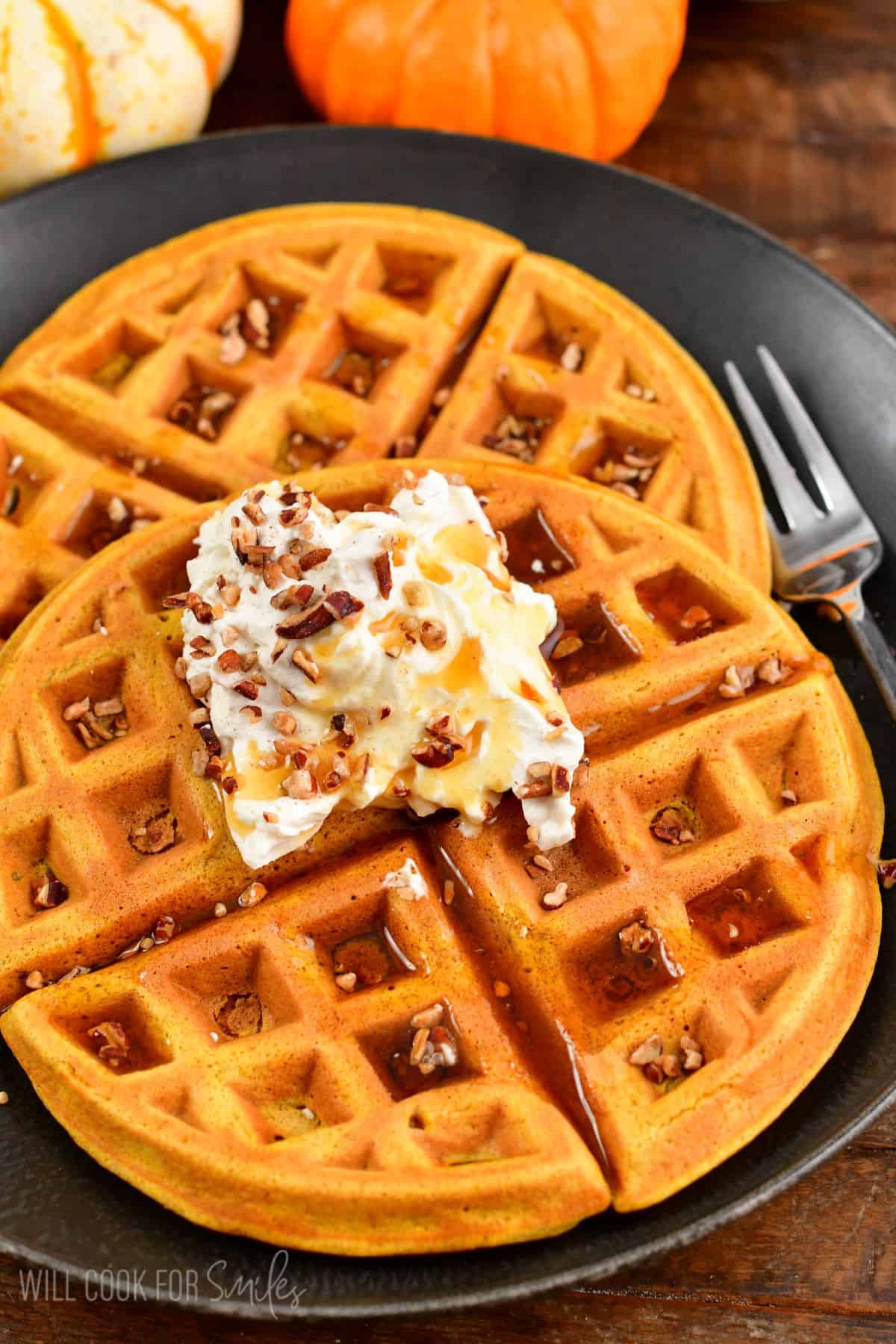 Two waffles on a plate with whipped cream and nuts on top and a fork to the right.