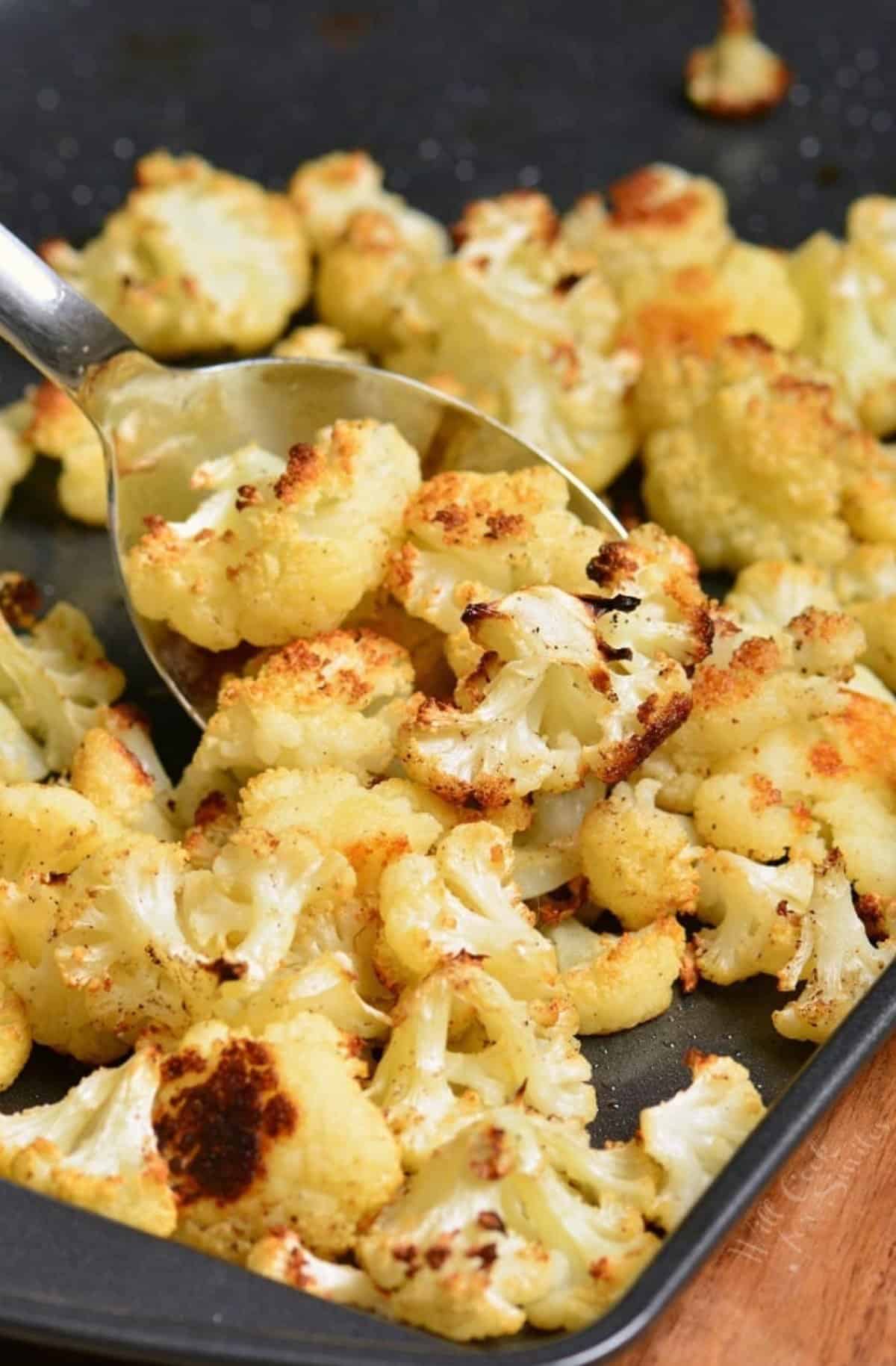 Roasted cauliflower on a baking sheet with a spoon scooping some up.