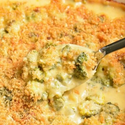 spooning some broccoli cheese casserole out of the baking dish with silver spoon.