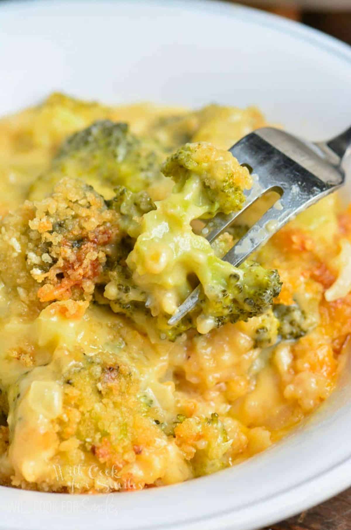 scooping some broccoli cheese casserole from the bowl with a fork.