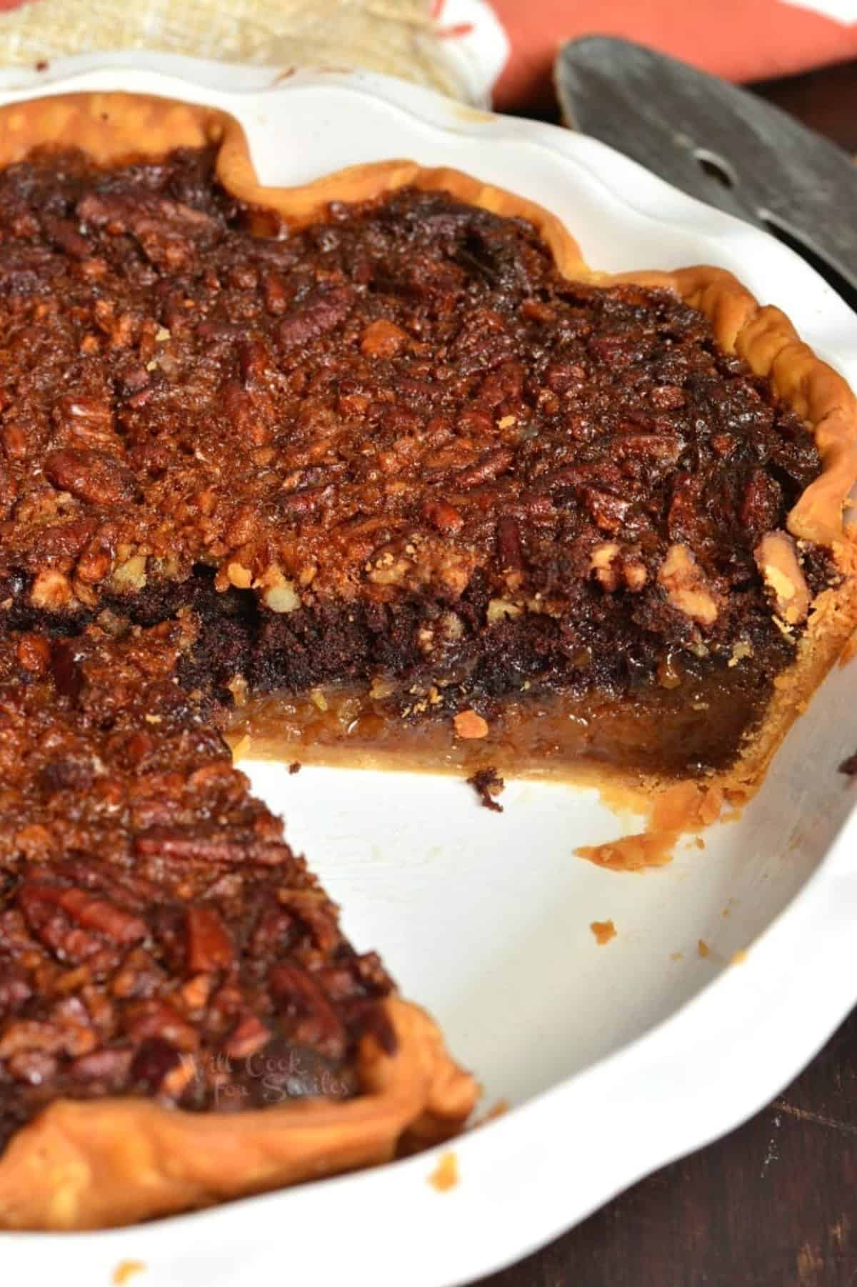 whole brownie pecan pie in the pie baking dish with one slice taken out.