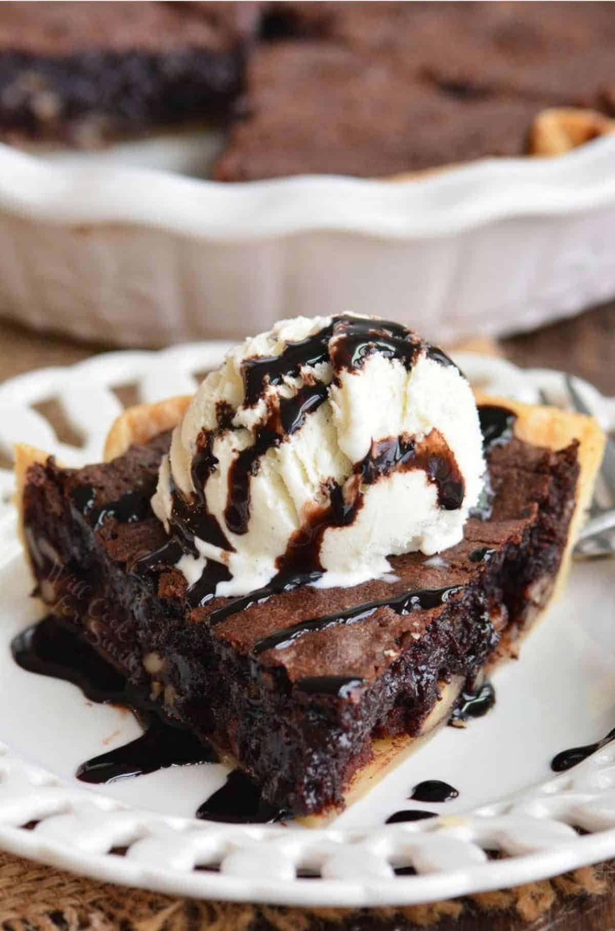 a slice of brownie pie topped with ice cream and chocolate syrup on a white plate.