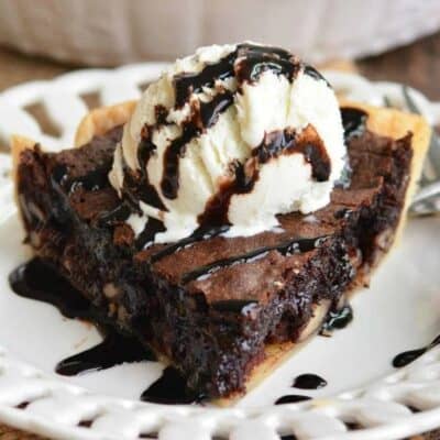 a slice of brownie pie on a plate topped with ice cream and drizzled with chocolate syrup.