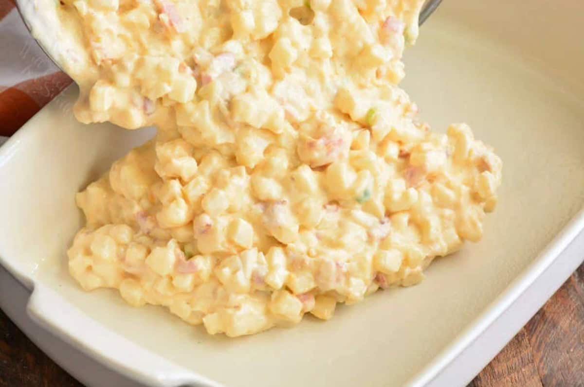 Pouring cheesy potato casserole into a baking dish.