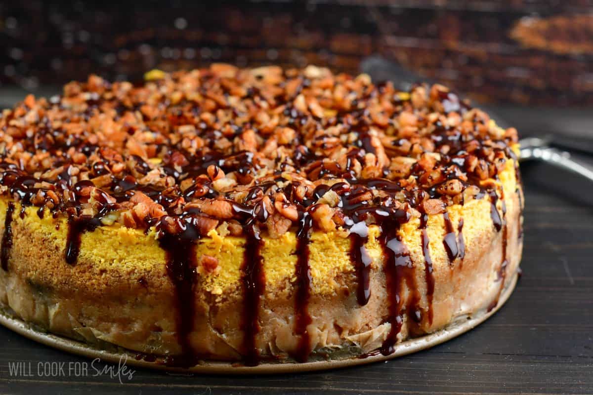 baked pumpkin cheesecake topped with pecans and chocolate drizzle.