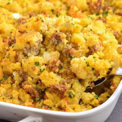 scooping sausage cornbread dressing from the baking dish with a silver spoon.