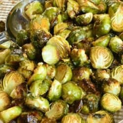 Garlilc butter roasted brussels sprouts on a baking sheet with a metal serving spoon scooping some up.