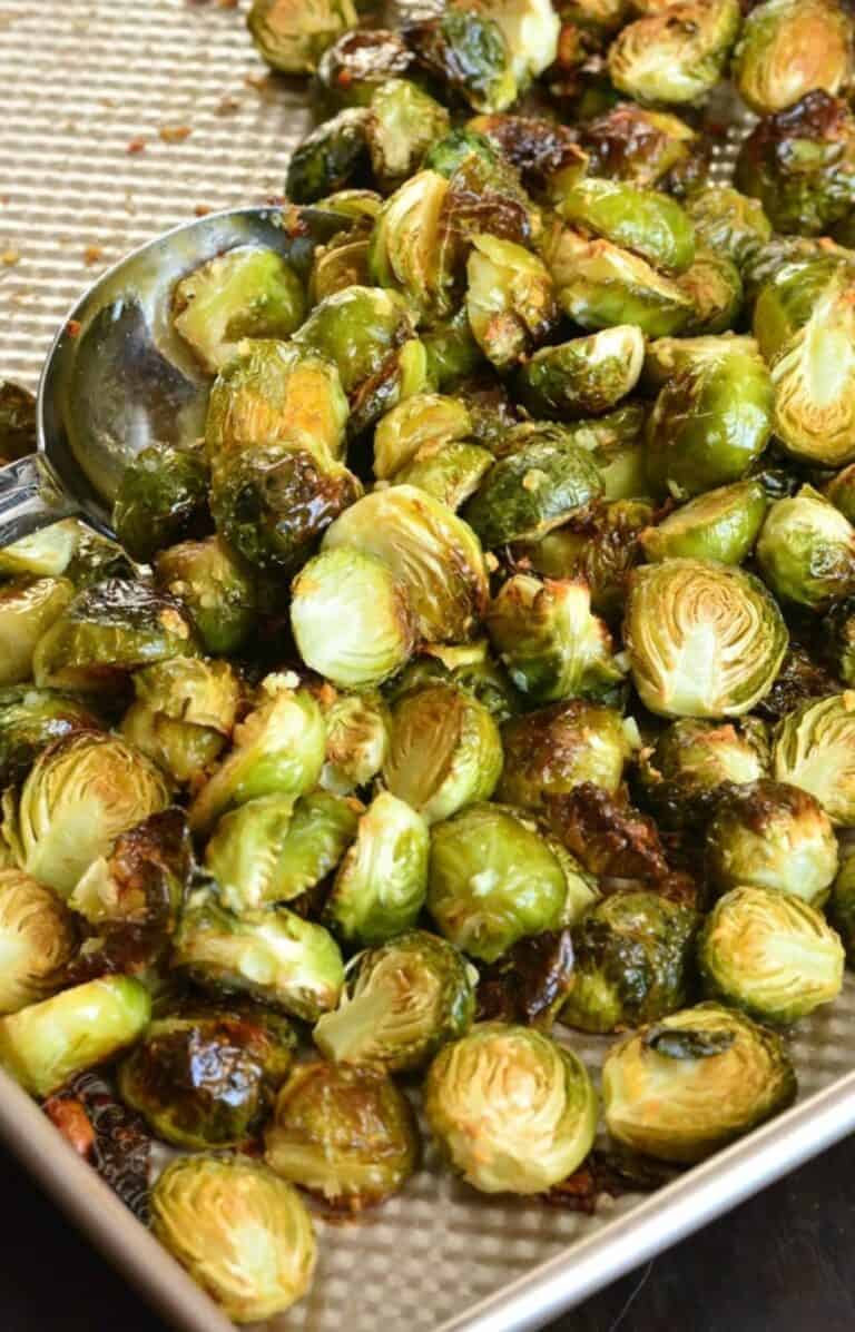 Garlilc butter roasted brussels sprouts on a baking sheet with a metal serving spoon scooping some up.