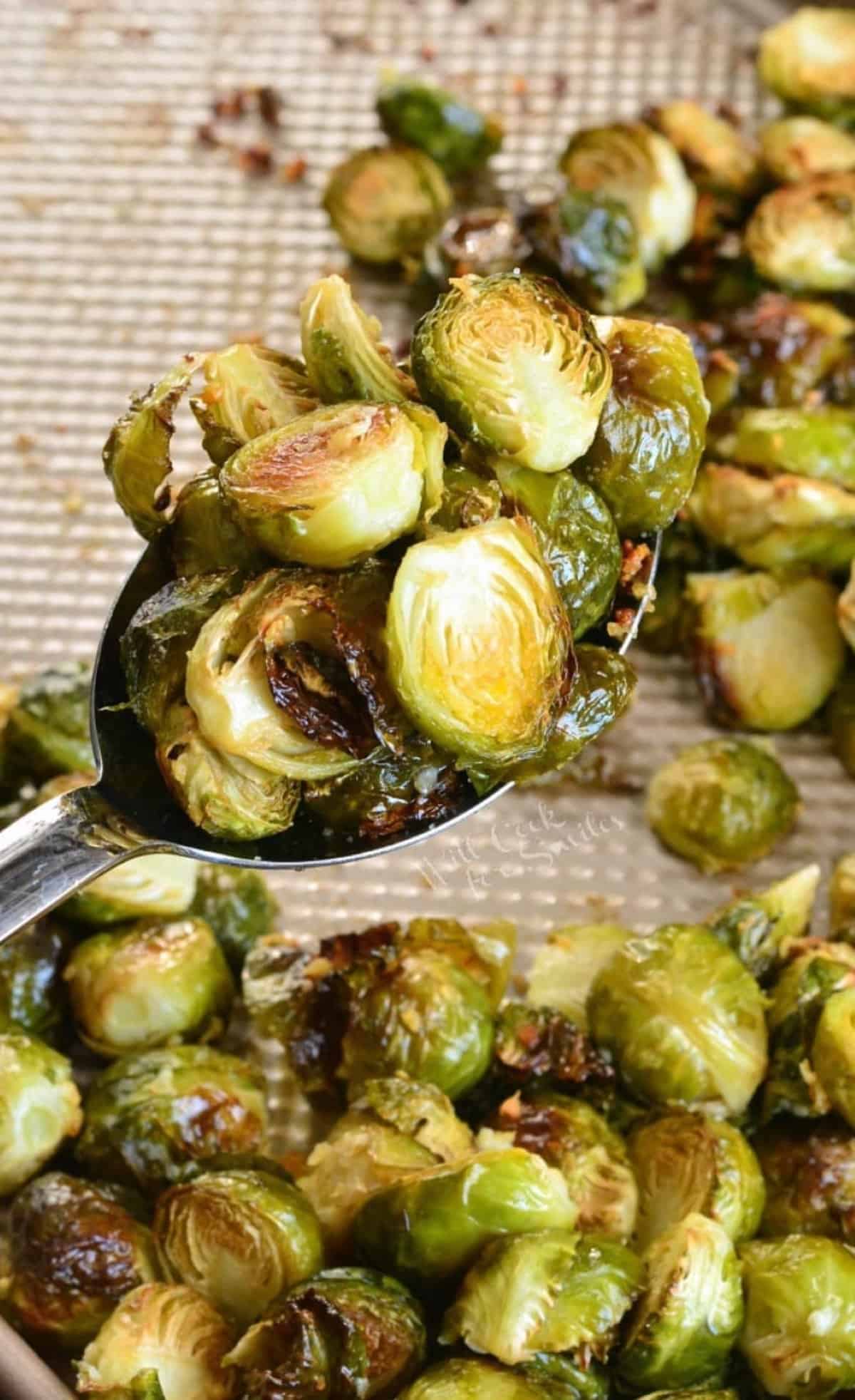 Garlic butter roasted brussels sprouts scooped up with a spoon and the rest on a baking sheet.