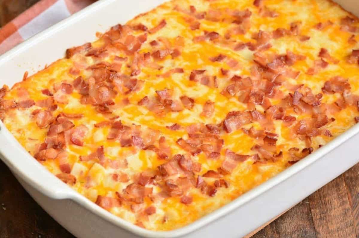 Cooked loaded cheesy potatato casserole in a baking dish on a wood surface.