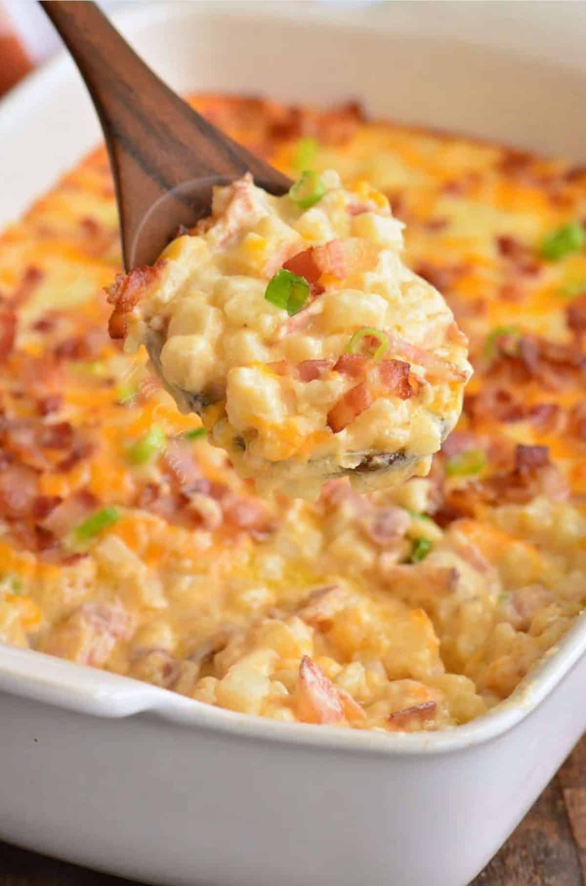 Loaded cheesy potato casserole scooped onto a wooden spoon.