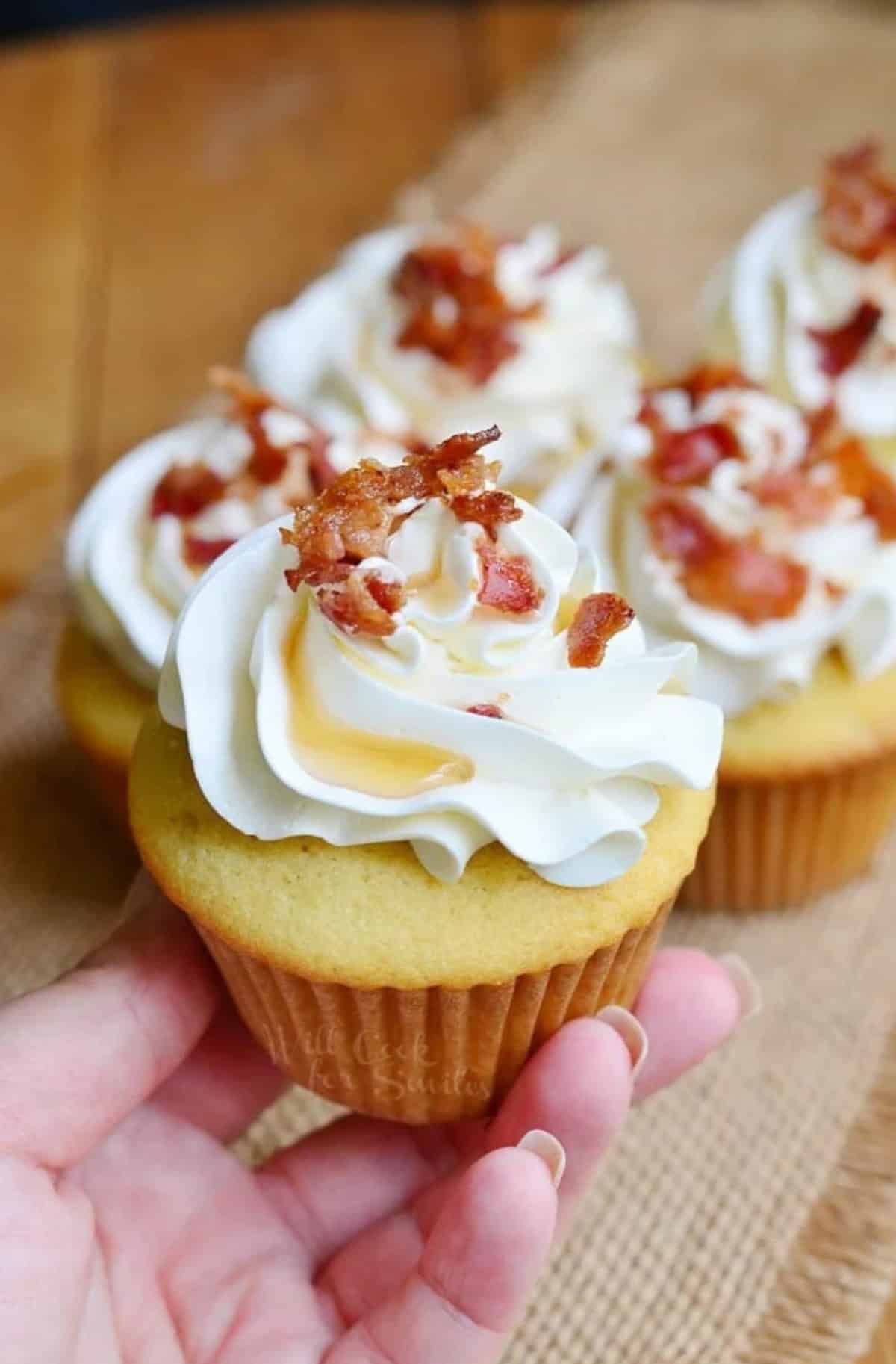 holding one maple bacon cupcake with buttercream frosting.