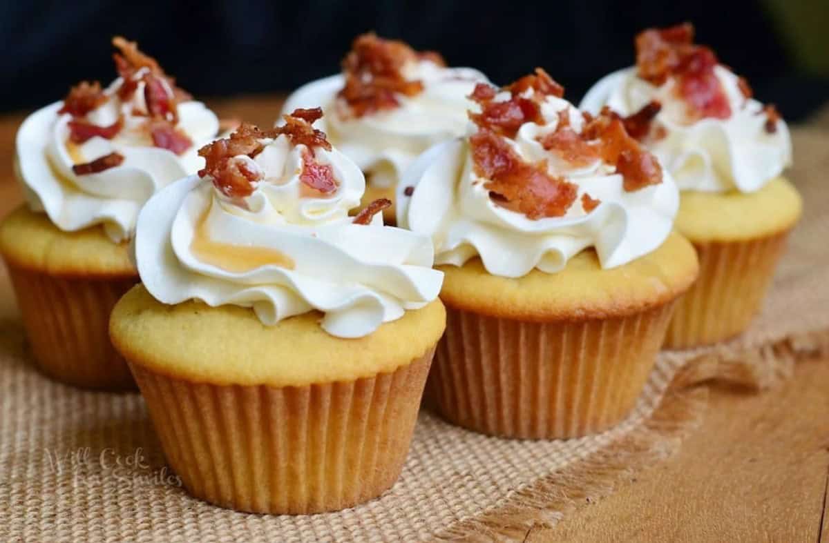 several maple bacon cupcakes side by side topped with buttercream frosting and bacon bits.