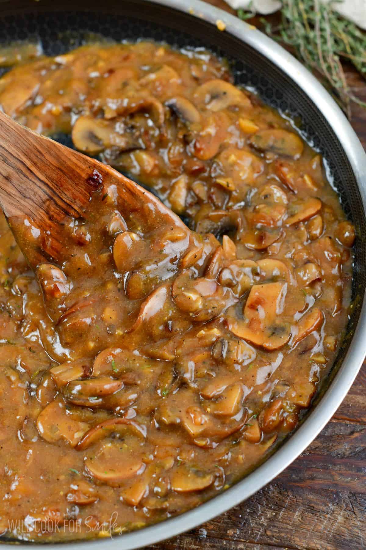 scooping mushroom gravy with a wooden spoon from the cooking pan.