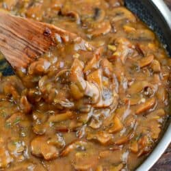 stirring the mushroom gravy with a wooden spoon in the pan.