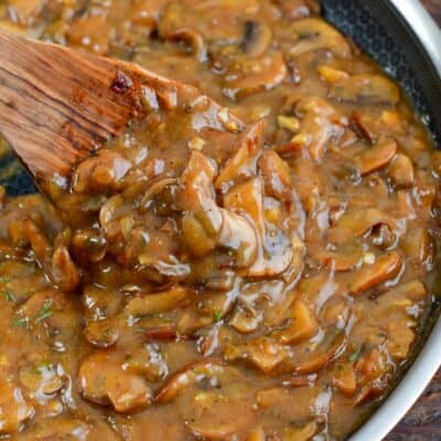 stirring the mushroom gravy with a wooden spoon in the pan.