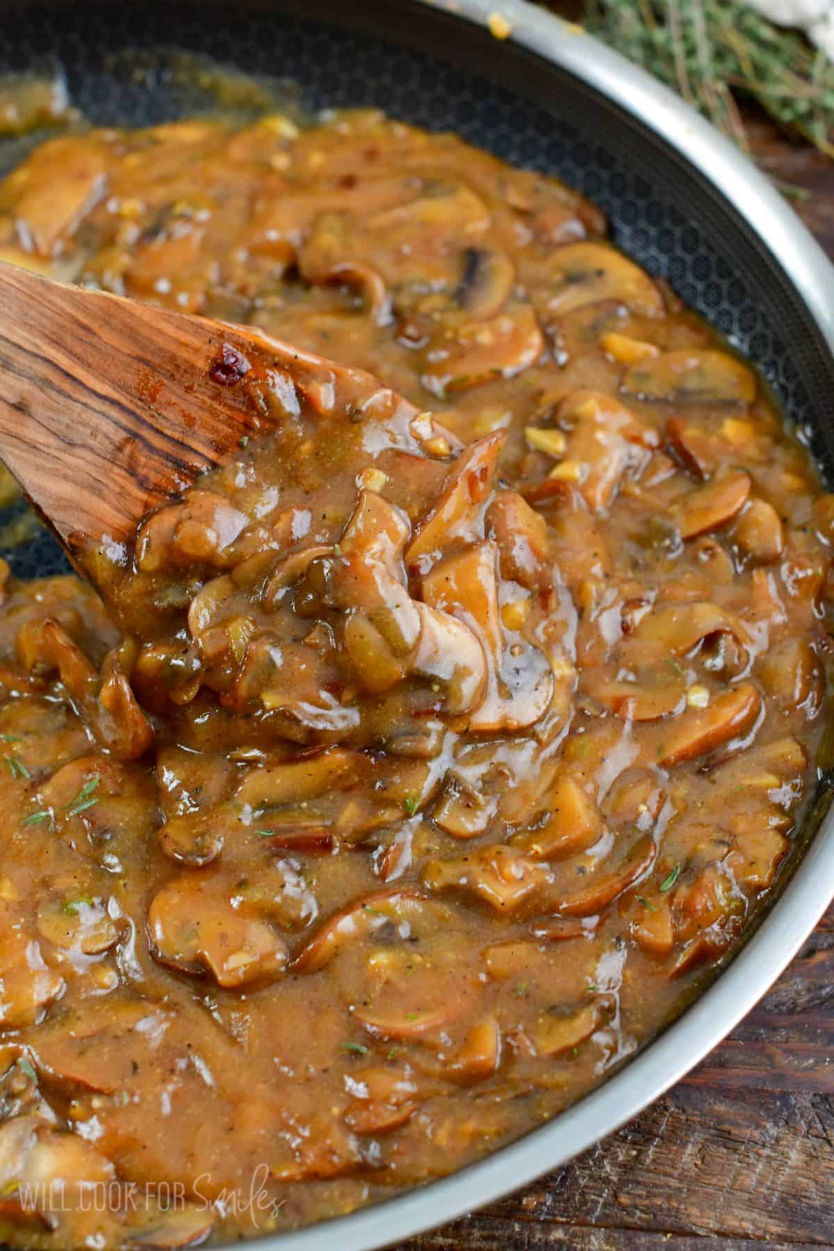 stirring the mushroom gravy with a wooden spoon in the pan.