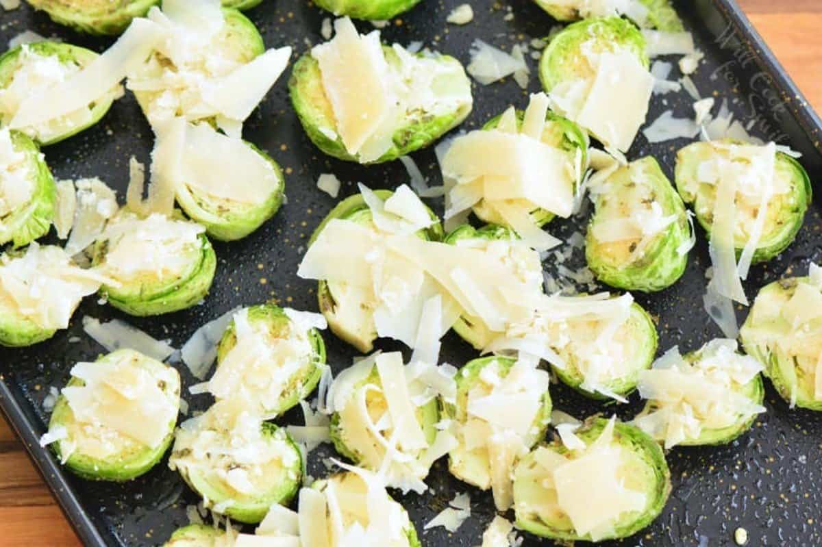 Brussels sprouts spread out on a baking sheet with parmesan on top of them.