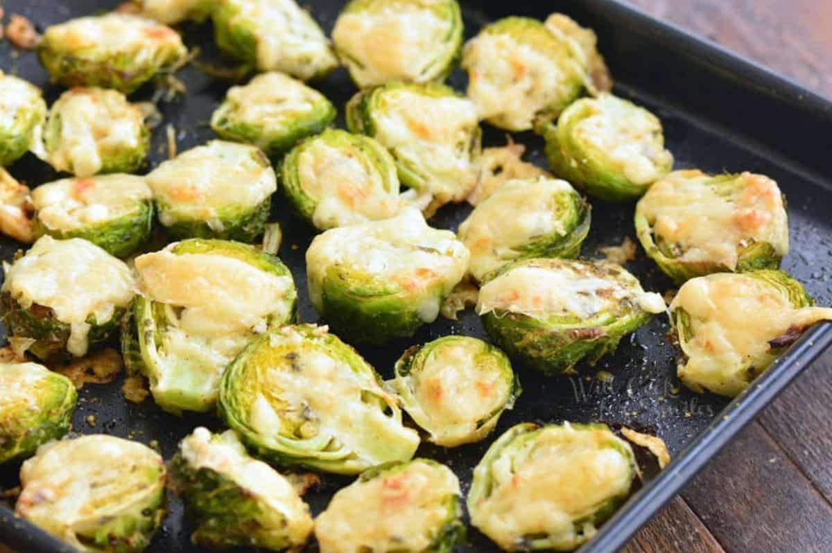 Roasted brussel sprouts on spread out on a baking sheet with cheese melted on top.