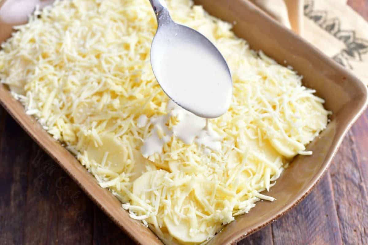 Adding heavy cream over potaoes and cheese in a baking dish.