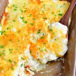 scalloped poatoes in a baking dish with a some taken out and a wooden spoon scooping some.