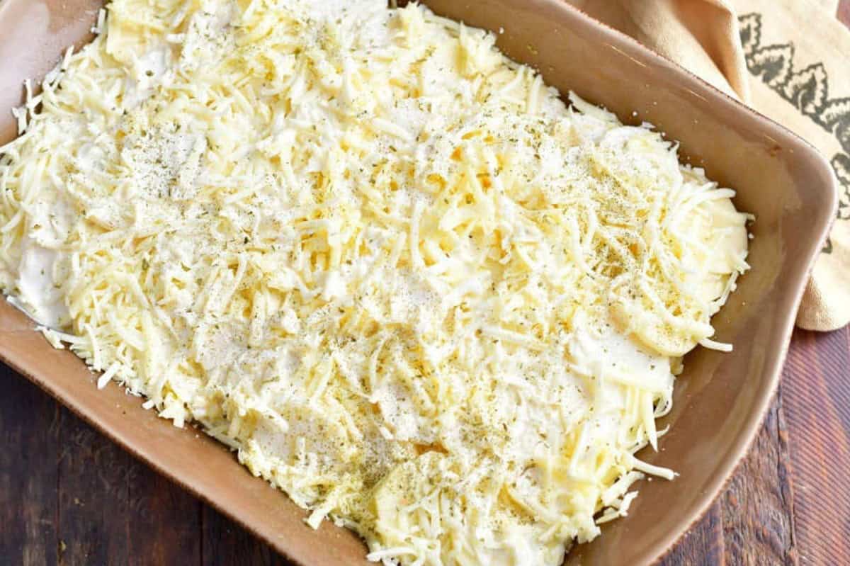 Uncooked scalloped potatoes in baking dish with shredded cheese on top.