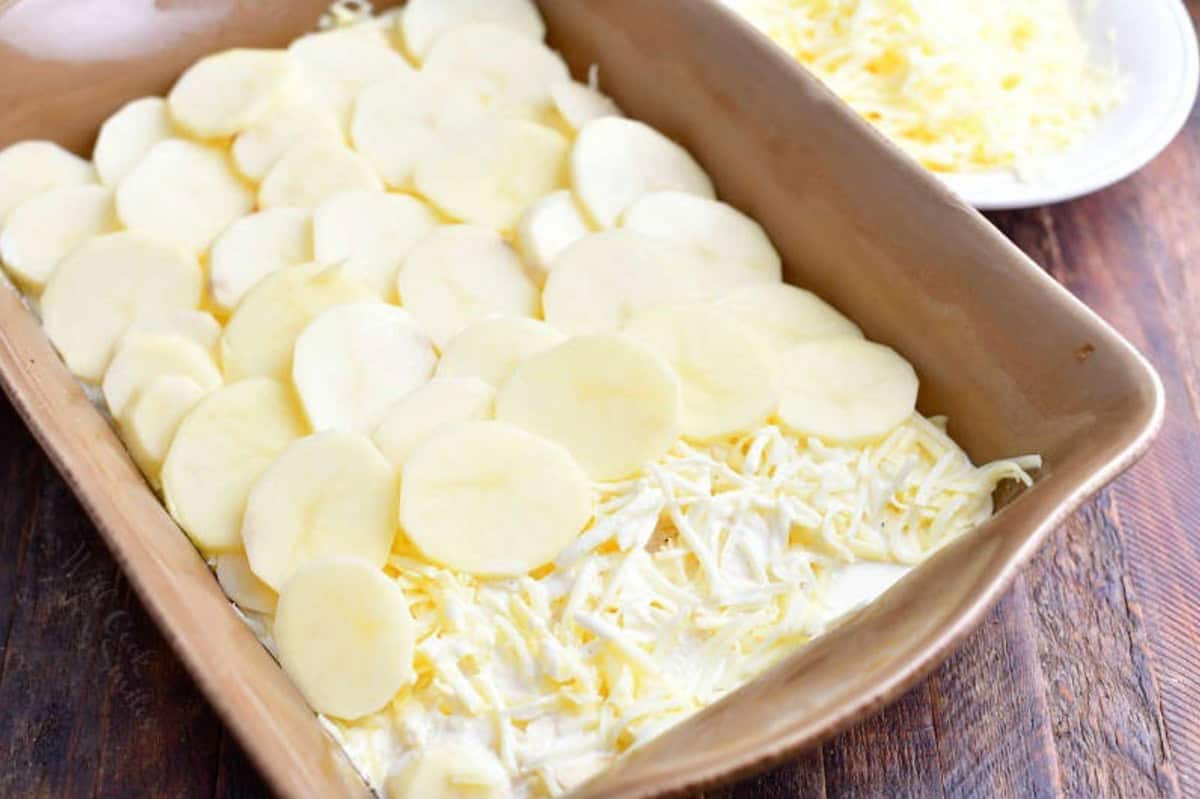 Layering potatoes, cheese, and cream in a baking dish.