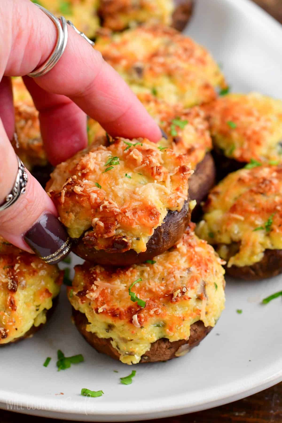 holding one stuffed mushroom cap on top of other over the platter.